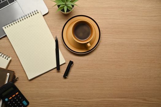 Top view of coffee cup, blank notepad, calculator and laptop computer on wooden table.