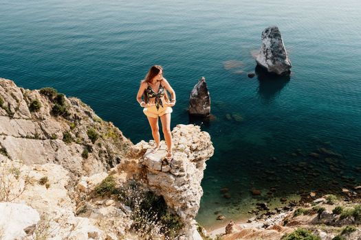 Woman travel sea. Happy tourist taking picture outdoors for memories. Woman traveler looks at the edge of the cliff on the sea bay of mountains, sharing travel adventure journey.