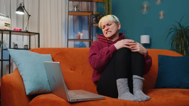 Displeased woman with short blonde hair use laptop typing browsing working, loses becoming surprised sudden lottery results bad news, fortune loss fail. Adult girl at home in evening room on couch