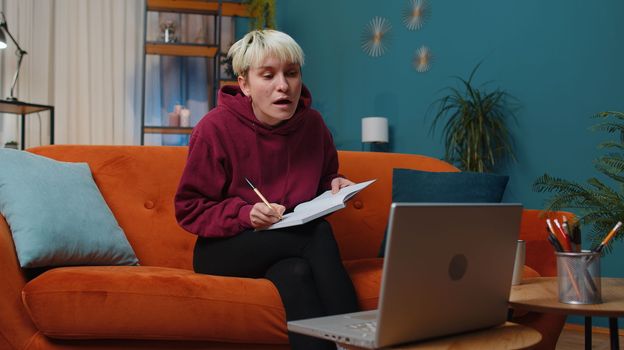 Woman with short hair freelancer teacher study with notebook sitting on sofa at home. Girl conference video call talking to webcam at night room. Online e-learning in remote chat. Distance education