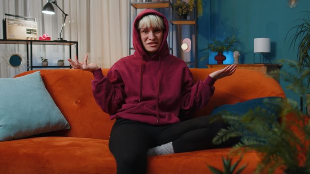 What. Why. Woman with short hair raising hands in indignant expression asking reason of failure demonstrating disbelief irritation by troubles at home apartment. Girl in evening room sitting on sofa