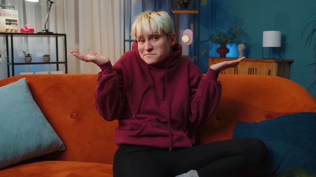 I dont know what to say. Confused young woman feeling embarrassed about ambiguous question, having doubts, no idea, being clueless uncertain at home. Girl at night living room. Lgbt gay lesbian people
