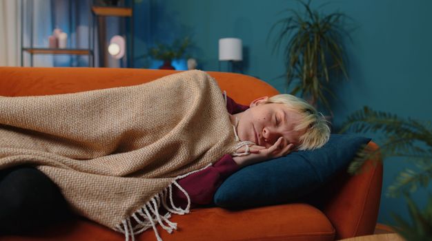 Tired young woman with short blonde hair lying down in bed taking a rest at home room. Carefree girl napping, falling asleep on comfortable sofa with pillows. Closed her eyes enjoy night nap alone