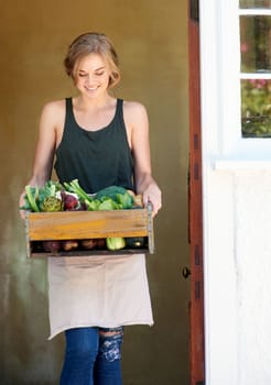 Good for nature, good for you. A young woman holding a crate of vegetables outdoors