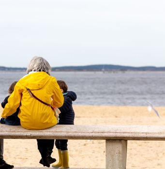 senior woman sitting on a bench by the beach with her little children