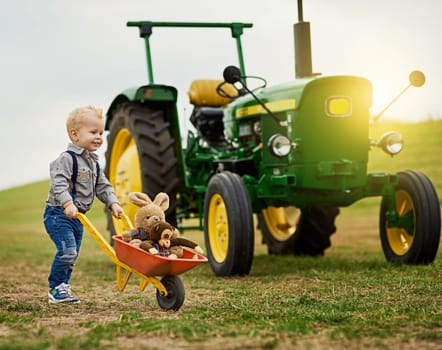 Rounding up the livestock like a champ. an adorable little boy pushing a toy wheelbarrow filled with stuffed animals on a farm