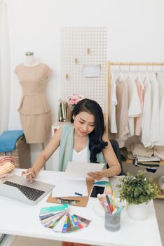 Fashion designer at work. Happy young Asian woman drawing while sitting at her working place in fashion workshop