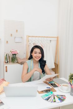 Fashion designer at work. Happy young Asian woman drawing while sitting at her working place in fashion workshop