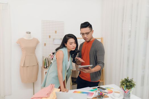 Two young woman and man fashion designers working and using tablet together at the studio