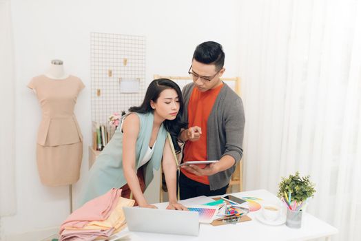 Two young woman and man fashion designers working and using tablet together at the studio