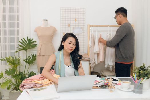 Fashion designers at work.  Handsome male designer choosing design while his colleague working with laptop.