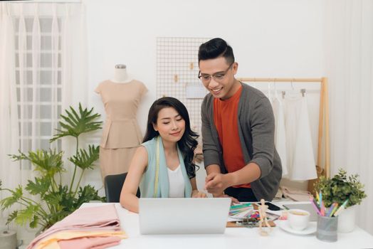 Couple of Asian fashion designer is working together while they using laptop to find something