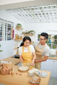 Couple man and woman wearing aprons having fun while making homemade pasta in kitchen at home