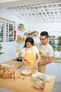 Couple man and woman wearing aprons having fun while making homemade pasta in kitchen at home