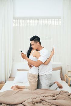 Young couple in the bedroom. Side view of unfaithful man and woman are cheating on the phone while hugging each other