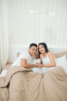 Young asian couple smile listen music with smart mobile phone on bed at bedroom with fun and enjoy