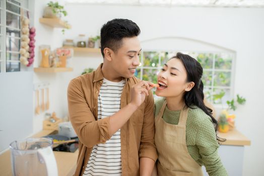 Beautiful happy asian couple are feeding each other in the kitchen.