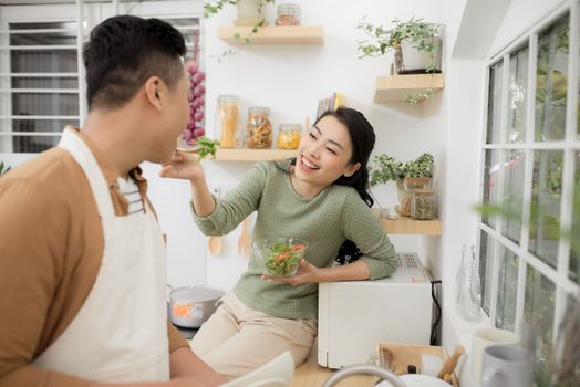 Loving woman feeding man while cooking dinner at kitchen.