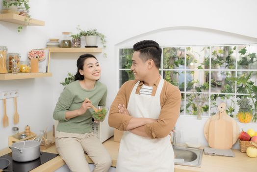 Happy young couple eating and talking in the kitchen