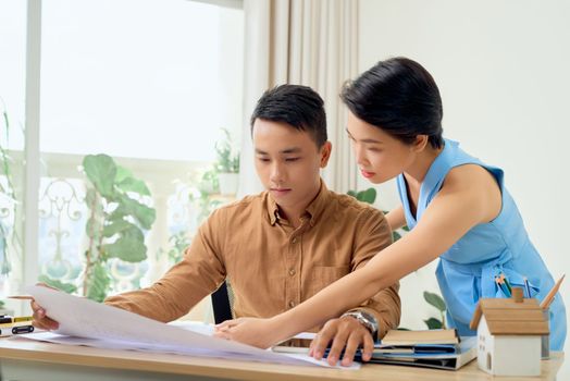 Finding solution together. Confident young man and woman looking at blueprint together while both standing in office