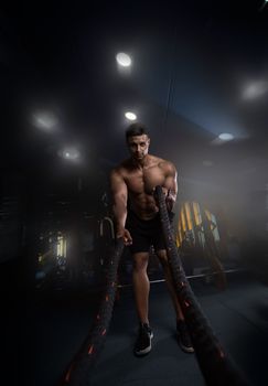 Muscular guy working out with ropes in the gym without a t-shirt, creative photo, without clothes, a handsome guy, will erase into the camera lens, beautiful body, physique, relief, sexy guy.