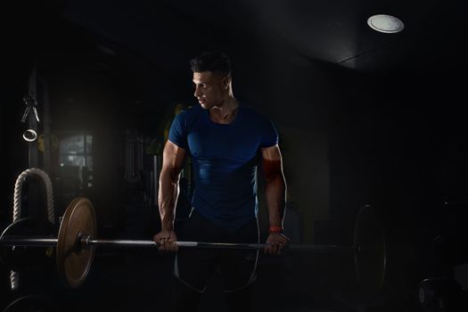 a man lifts weights in the gym and looks to the side in a tight t-shirt, creative photo