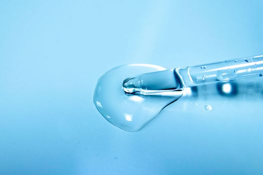 Water bubbles with cosmetic liquid drops of serum on a blue background of a laboratory glass pipette. Close-up of a pipette with drops.