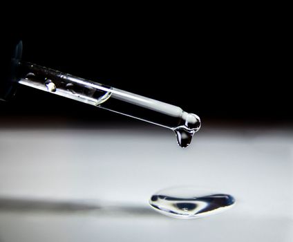 Liquid transparent gel drips from a serum pipette with drops on a light background. Close-up.