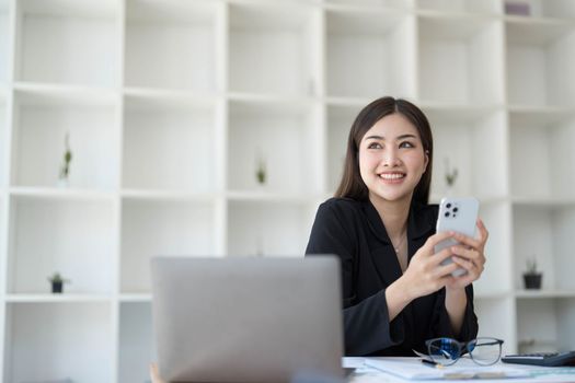 Smiling beautiful Asian businesswoman analyzing chart and graph showing changes on the market and holding smartphone at office...