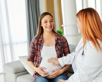 Portrait of a young happy pregnant woman doing exam with doctor or nurse during a visit at home or in a clinic