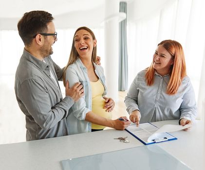 Young happy couple, a pregnant woman, and an agent in a new property