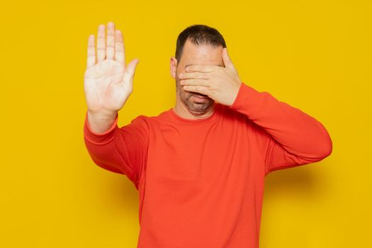 Handsome hispanic man wearing red jumper over isolated yellow background covering eyes with hands and doing stop gesture with sad and afraid expression. Embarrassed and negative concept.