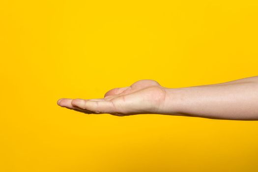 Strong hand of man with palm up presenting an imaginary product in advertising concept isolated on yellow background