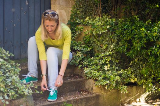 Young blonde girl ties up shoelaces on green sneakers