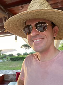 Smiling man in sunglasses and a straw hat is standing in the garden. Portrait. High quality photo