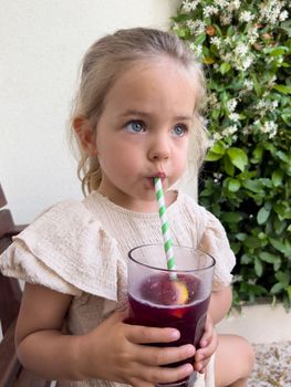 Little girl drinks cold juice from a glass through a straw. High quality photo