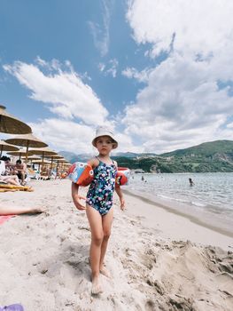 Little girl in inflatable armlets stands on the beach . High quality photo
