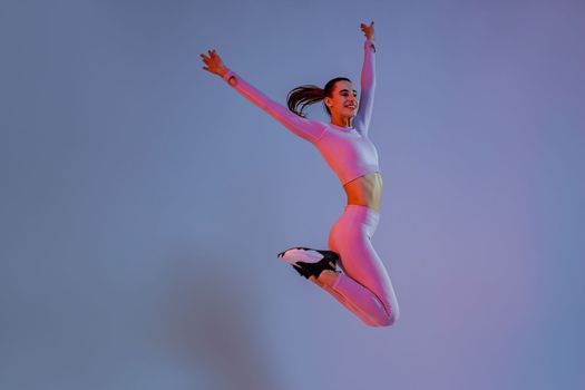 Athletic active woman jumping on studio background with colored filter. Dynamic movement