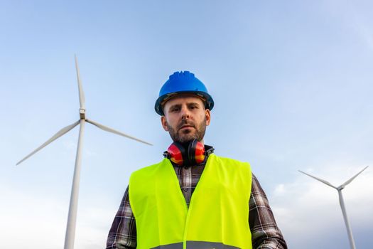 Maintenance worker standing at wind turbine farm looking at camera. Renewable energy concept.