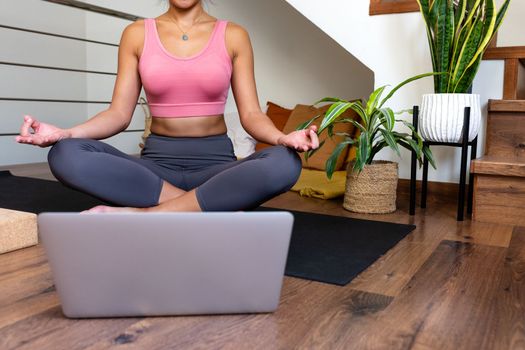 Unrecognizable young woman meditating at home with online video meditation lesson using laptop. Healthy lifestyle concept.