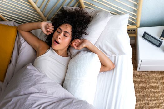 Young African American woman waking up in the morning, yawning and stretching arms in bed. Good morning. Lifestyle concept.