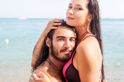 Close up shot of beautiful young caucasian woman with black hair and freckles looking at camera and smiling. Cute woman portrait in a pink bikini posing on a volcanic rock high above the sea