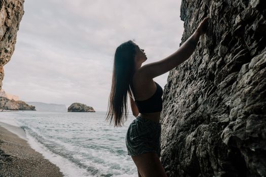 A girl climbs a rock. The athlete trains in nature. Woman overcomes difficult climbing route. Extreme hobby. Tourist woman rock climber hiking on mountains rocks over beautiful sea coast