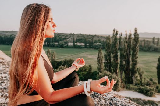 Well looking middle aged woman with long hair, fitness instructor in leggings and tops doing stretching and pilates on the rock near forest. Female fitness yoga routine concept. Healthy lifestyle.