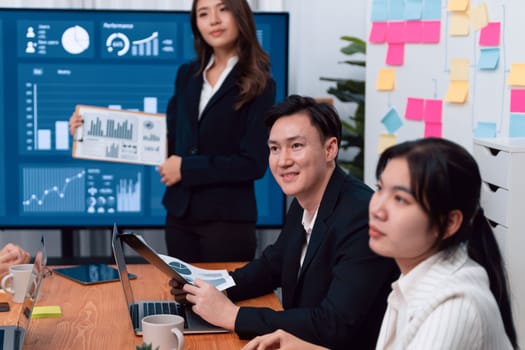 Confidence and young asian businesswoman give presentation on financial business strategy in dashboard report display on screen to colleagues in conference room meeting as harmony in workplace concept