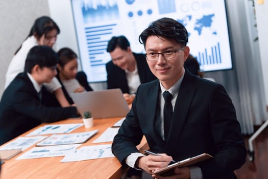 Focus portrait of successful confident male manager or executive in business wear with blurred background of businesspeople, colleagues working with financial report papers in office of harmony.