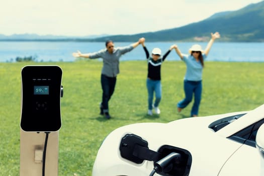Concept of progressive happy family enjoying their time at green field and lake with electric vehicle. Electric vehicle driven by clean renewable from eco-friendly power sauce.