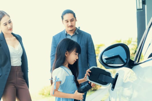 Focus closeup electric vehicle recharging battery from home electric charging station with blurred family in background. Renewable clean energy car for progressive eco awareness lifestyle concept.