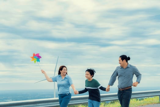Progressive happy family enjoying their time at wind farm for green energy production concept. Wind turbine generators provide clean renewable energy for eco-friendly purposes.