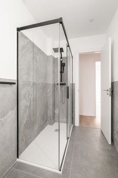 Bathroom with gray granite walls. The shower cabin is enclosed by glass transparent sliding doors in a black metal frame. Beautiful strict design is shown in accessories of black color